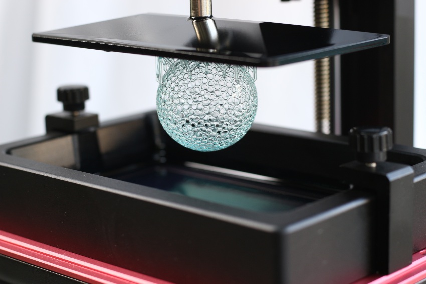A close-up of a sphere with a complex hole pattern, called a Voronoi pattern, which Dr. Daniel printed using an Additive Manufacturing process called stereolithography. In stereolithography the part is fabricated from a photopolymer resin.The sphere is shown just after the 3D printing process has finished, while it is still attached to the printing platform.