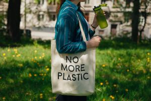 Woman walking, wearing a canvas bag that says NO MORE PLASTIC and holding a reusable water bottle.