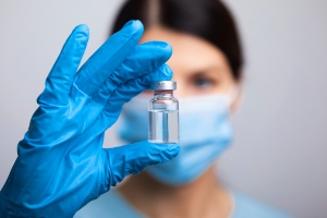 Woman wearing blue latex glove holding an unmarked vial.