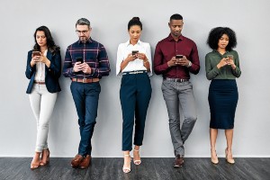 Diverse group of people leaning back against a wall looking at their phones
