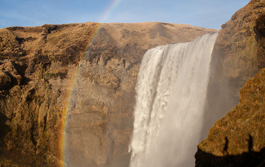 Landscape photo of a waterfall atop a mountain with a rainbow overlooking it