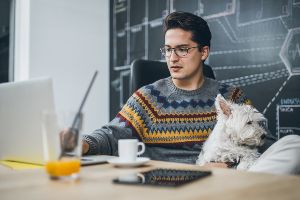 Man, mid-30s, sitting at desk with white dog in his lap, espresso in front of him.