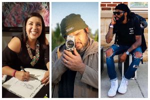 Three people pictured. Woman who is drawing and smiling. Man who is pointing his camera at us. Man sitting on DJ gear on the sidewalk.