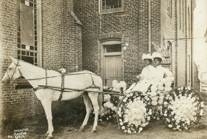 Two Black women dressed in all white sit atop a beautifully decorated Juneteenth carriage drawn by a white horse