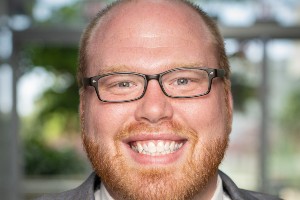 White man, red hair and beard with glasses, smiling