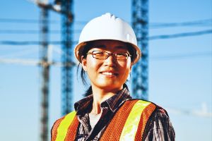 Young smiling woman wearing a hard hat and safety vest at a construction site.