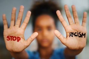 Young black girl holding up her hands with the words stop and racism on the palms of her hands.