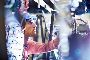 Man wearing a blue hardhat looks at wiring and other building infrastructure