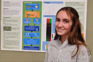 17 year year old girl, white, long medium brown hair, smiling in front of a science project poster.