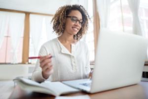 African American woman with open laptop, pen in hand, writing.