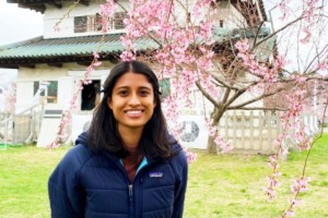 Young Indian woman smiling, standing in front of a blossoming cherry tree and a temple in Spring.