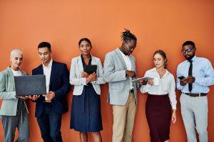 A group of diverse people leaning on a wall and chatting with each other.