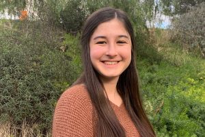 Young white woman with long, straight brown hair smiling at the camera.