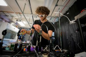 A student working in a lab wearing goggles and smiling