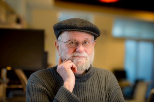 Older white man with a beard, glasses and a cap looking at the camera
