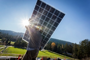 Man shouldering a solar panel as he prepares to install it on a house roof