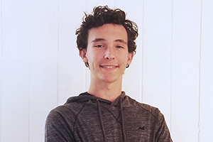 Young white male with curly brown hair smiles at the camera