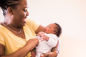 Haitian woman in her 20s tenderly holding a young infant in her arms.